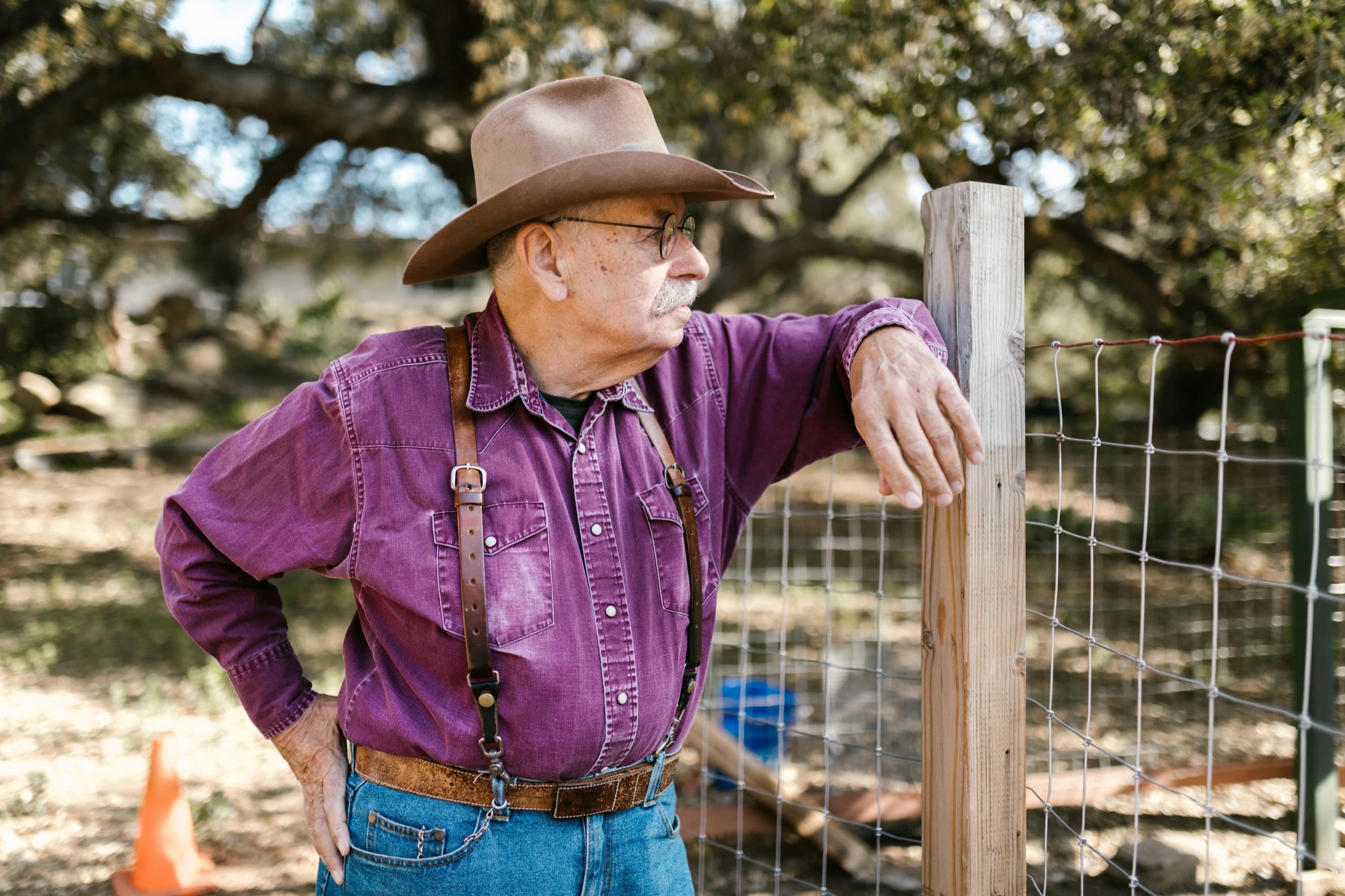 Texas rancher in cowboy hat tightening a wire fence at his property line